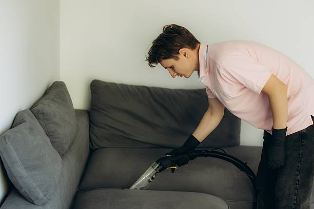seorang pria muda membersihkan sofa menggunakan vacuum cleaner
