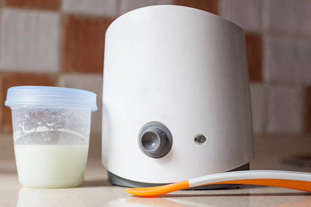 milk warmer dengan gelas mini dan sendok makan bayi di atas permukaan keramik