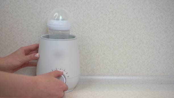 seseorang menggunakan milk warmer untuk menghangatkan botol susu bayi