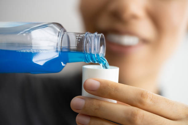 seseorang sedang menuangkan obat kumur ke tutup botolnya