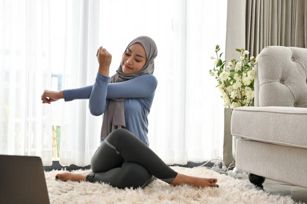 seorang wanita berhijab sedang stretching di area ruang tamu