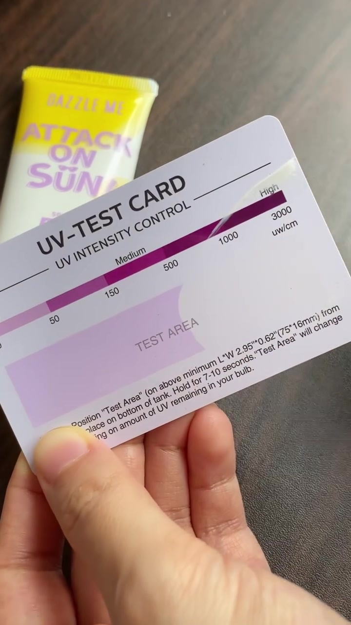 Tangan memegang kartu uji UV dengan tube sunscreen kuning di belakangnya, kartu dan tube memenuhi bingkai