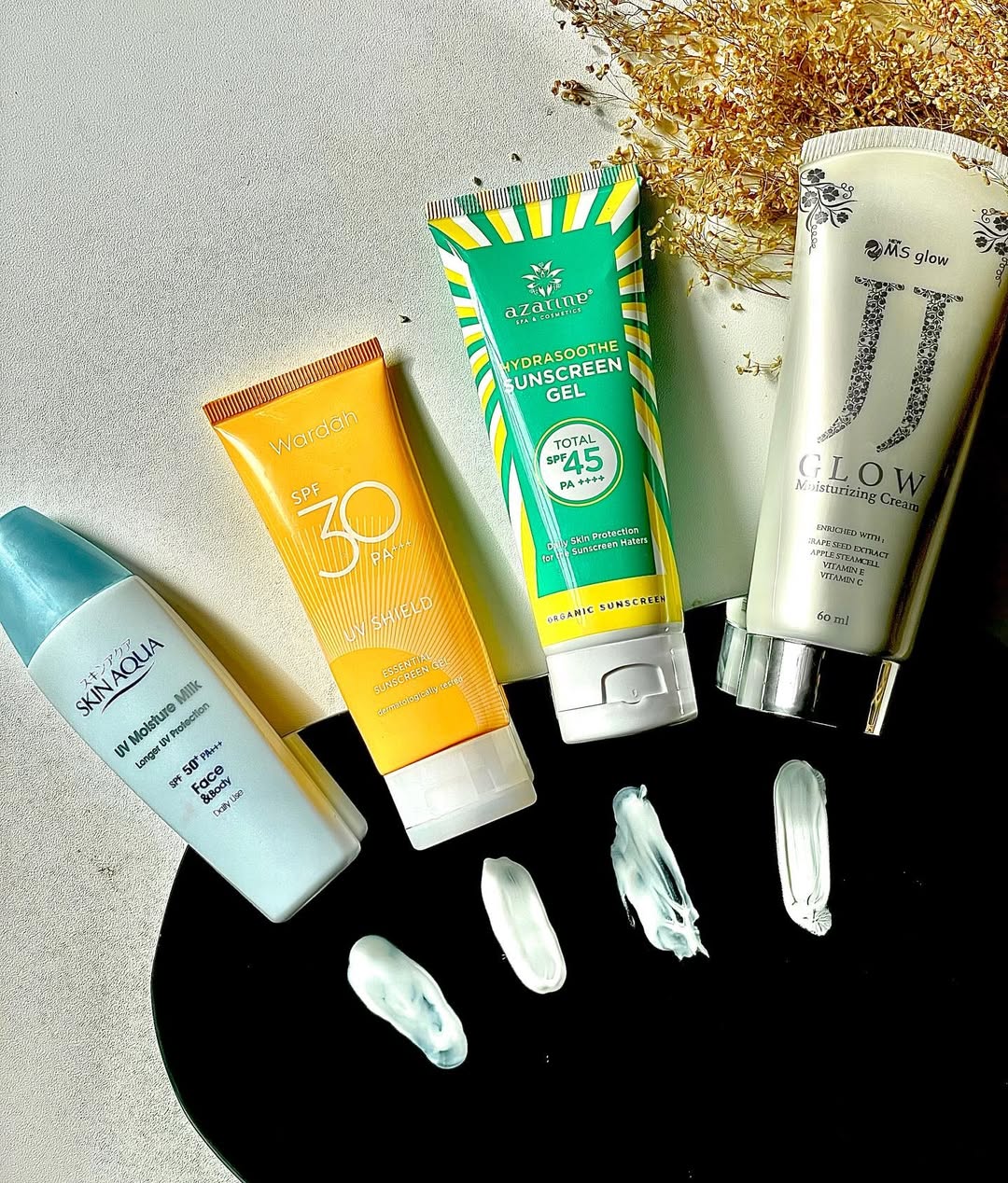 Empat tube sunscreen dari merek berbeda tersusun rapi berdampingan bersama swatch krimnya di permukaan gelap dan terang