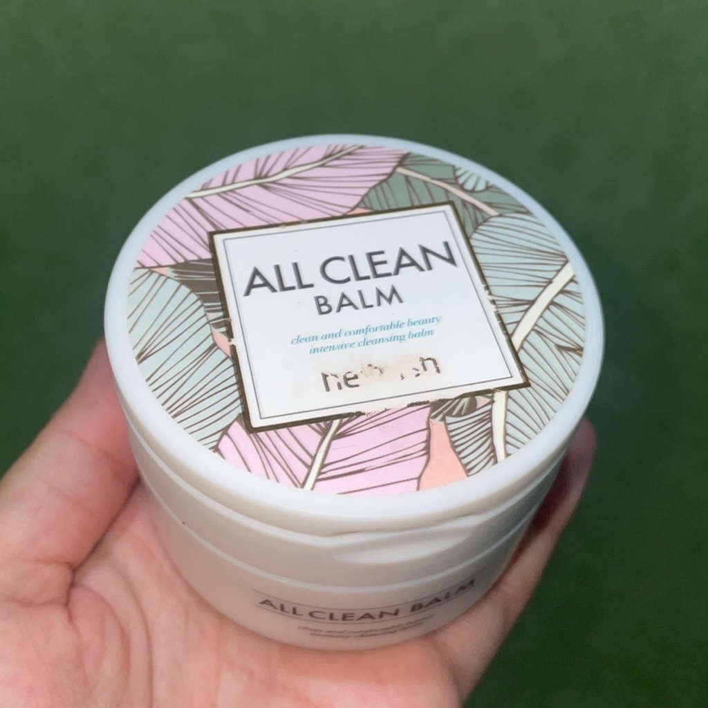 Jar Heimish All Clean Balm dengan tutup motif daun warna pink dan hijau dipegang di telapak tangan