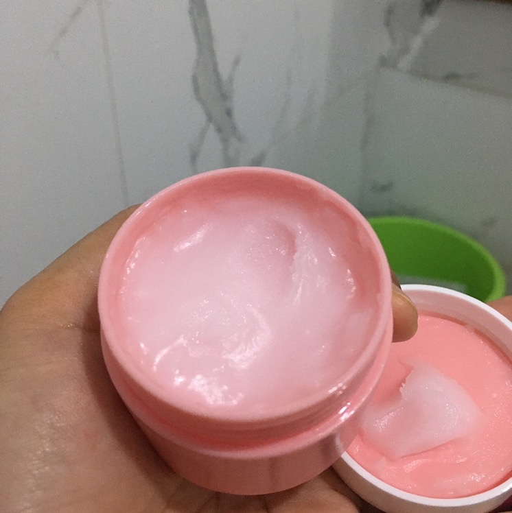 Tekstur cleansing balm merah muda yang mengilap di jar terbuka, dengan sedikit balm terscoops di bagian tutupnya