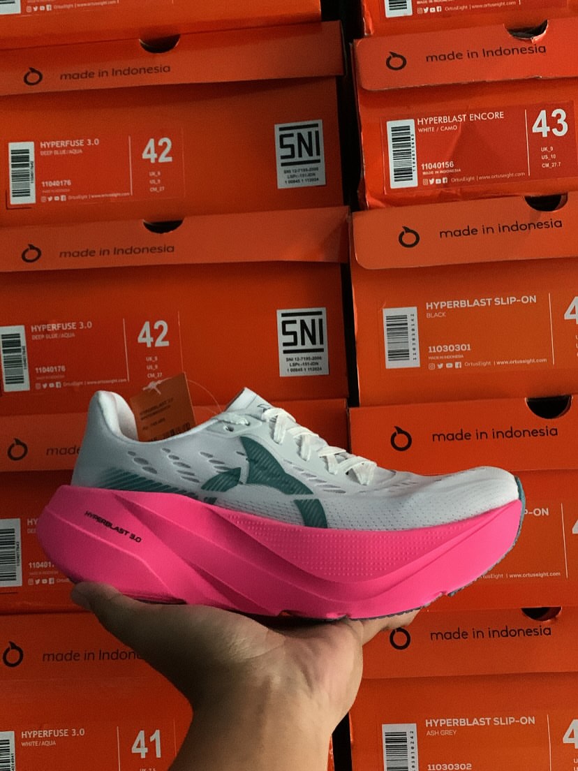 Ortuseight Hyperblast 3.0 warna putih-magenta dipegang di depan tumpukan kotak sepatu