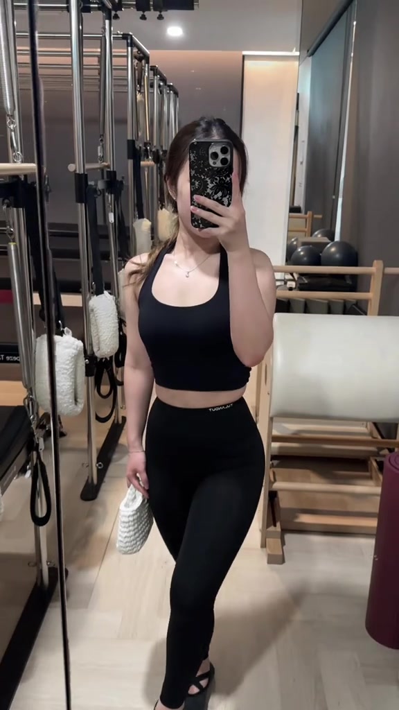 Try-on legging hitam high waist dan sport bra hitam di depan cermin studio pilates, wajah tertutup ponsel