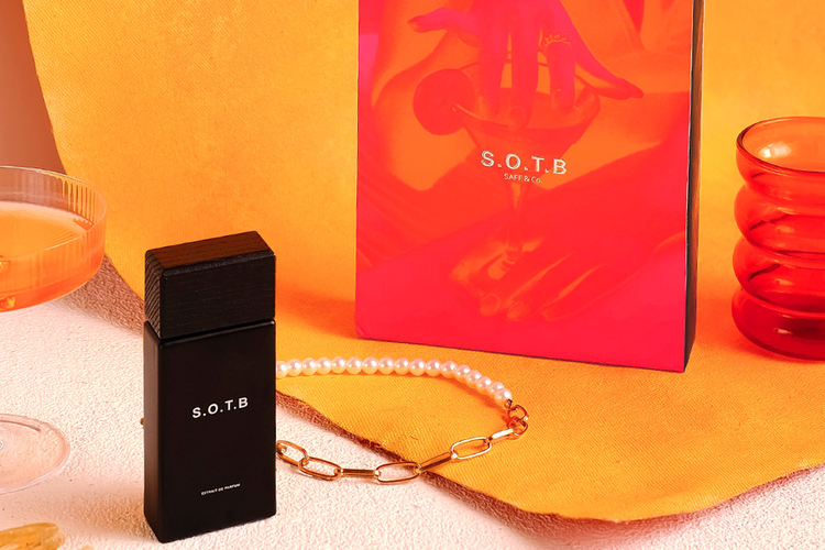 Botol parfum Saff & Co S.O.T.B berwarna hitam berdiri di depan kotak kemasan oranye dan merah muda