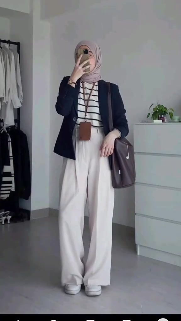 Selfie cermin dengan wajah tertutup ponsel: hijab dusty pink, blazer navy, inner salur putih hitam, celana putih lebar, sneakers putih, tas kulit cokelat, dan lanyard id card