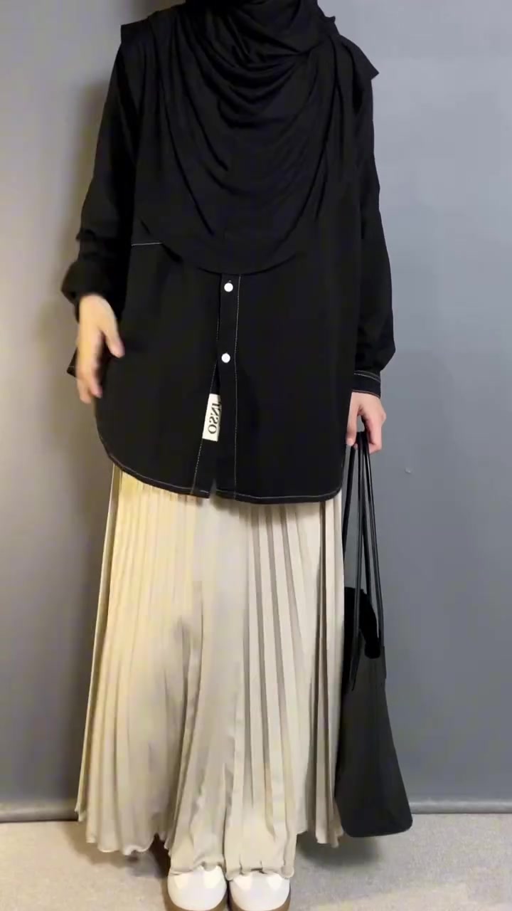 Kemeja hitam oversize dipadu rok plisket krem dan tote bag hitam, difoto dari leher ke bawah tanpa wajah