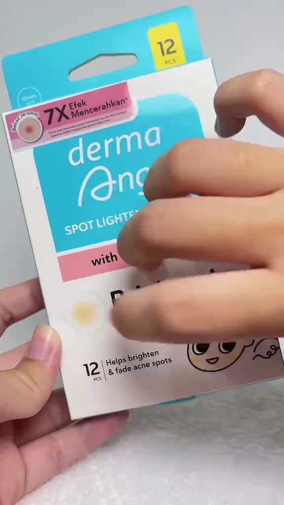 Tangan memegang kotak Derma Angel Spot Lightening Patch with TXA + CICA untuk bekas jerawat