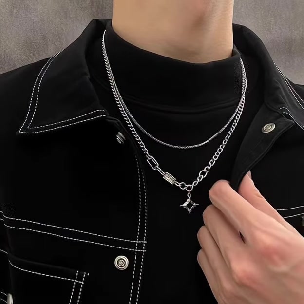 Dua kalung perak dengan panjang berbeda dipakai berlapis di atas turtleneck dan jaket hitam