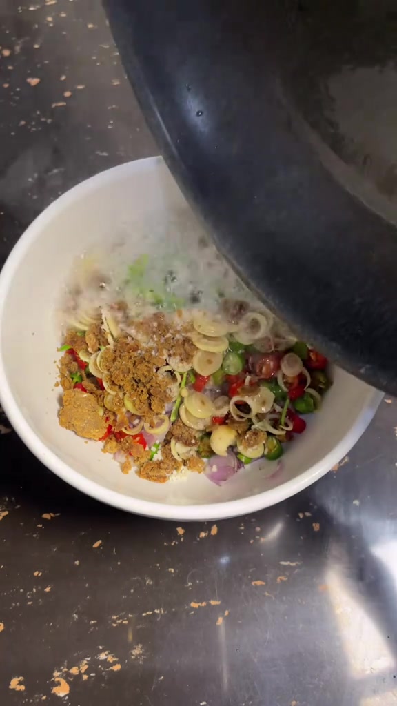 Minyak panas dituang dari wajan ke mangkuk berisi irisan cabe, bawang merah, dan serai