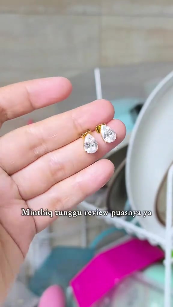 Jari memegang sepasang anting tusuk permata bentuk pir dengan rangka emas