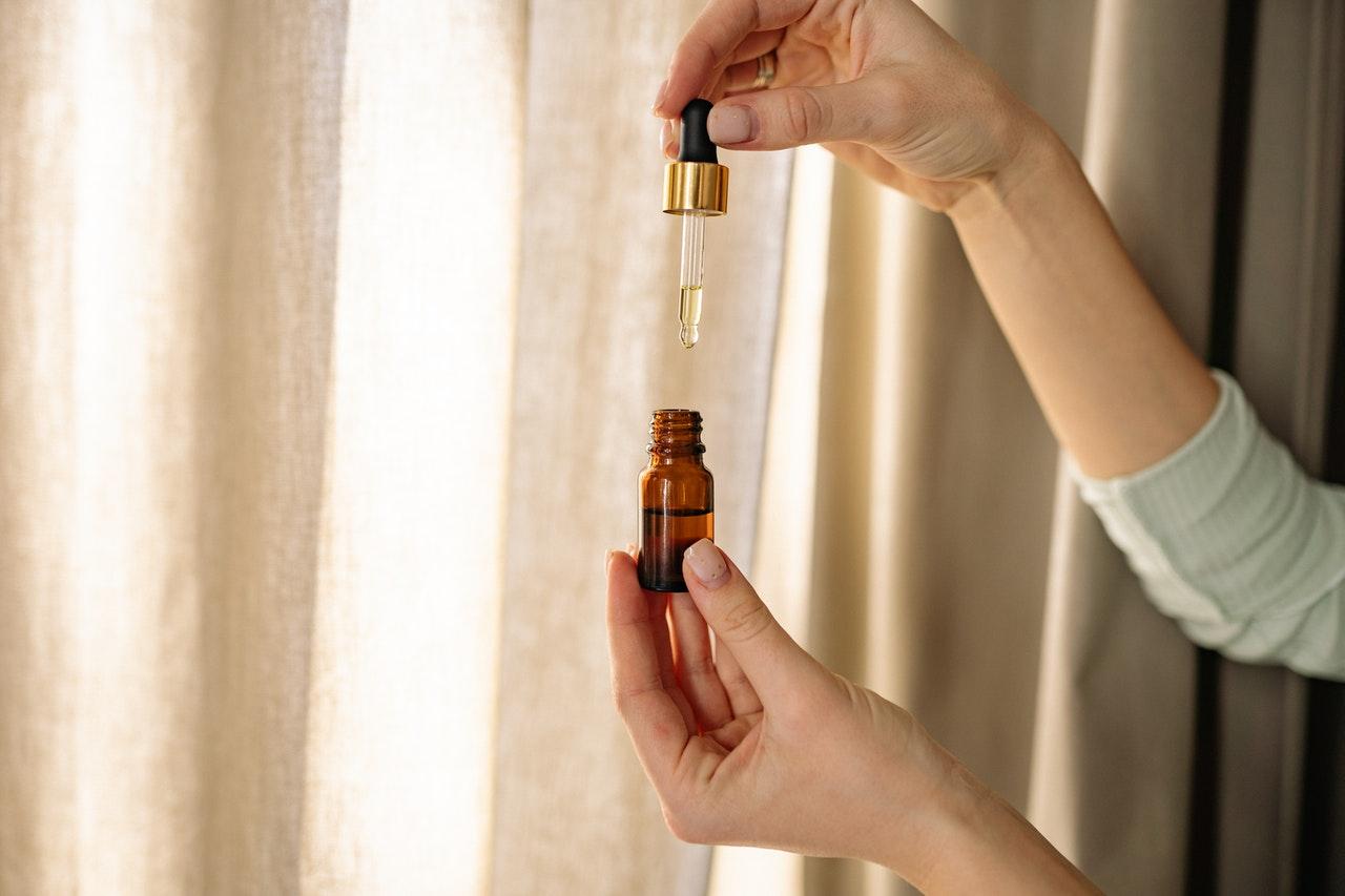 Tangan meneteskan oil dari dropper ke botol kaca amber kecil