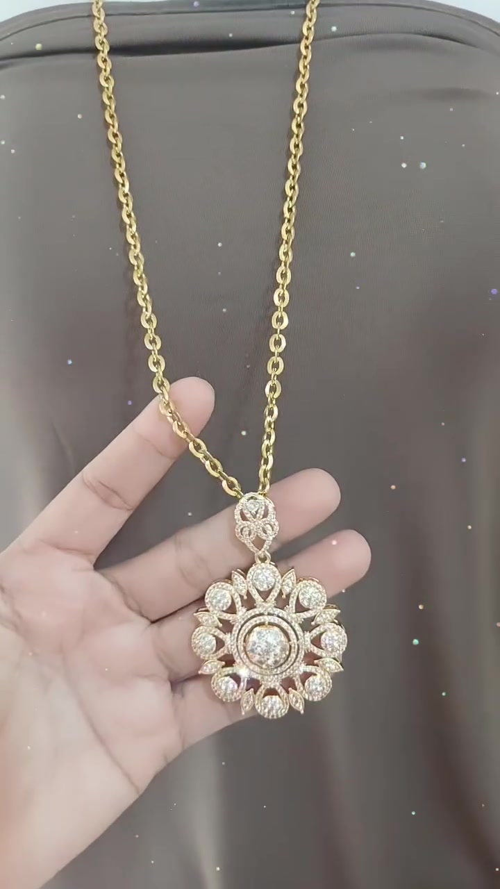 Kalung rantai gold dengan liontin bulat bertabur zircon dijuntai di telapak tangan di atas kain taupe