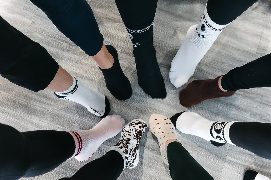 Beberapa pasang kaki peserta kelas pilates membentuk lingkaran di lantai studio, masing-masing memakai grip socks dengan warna dan model berbeda