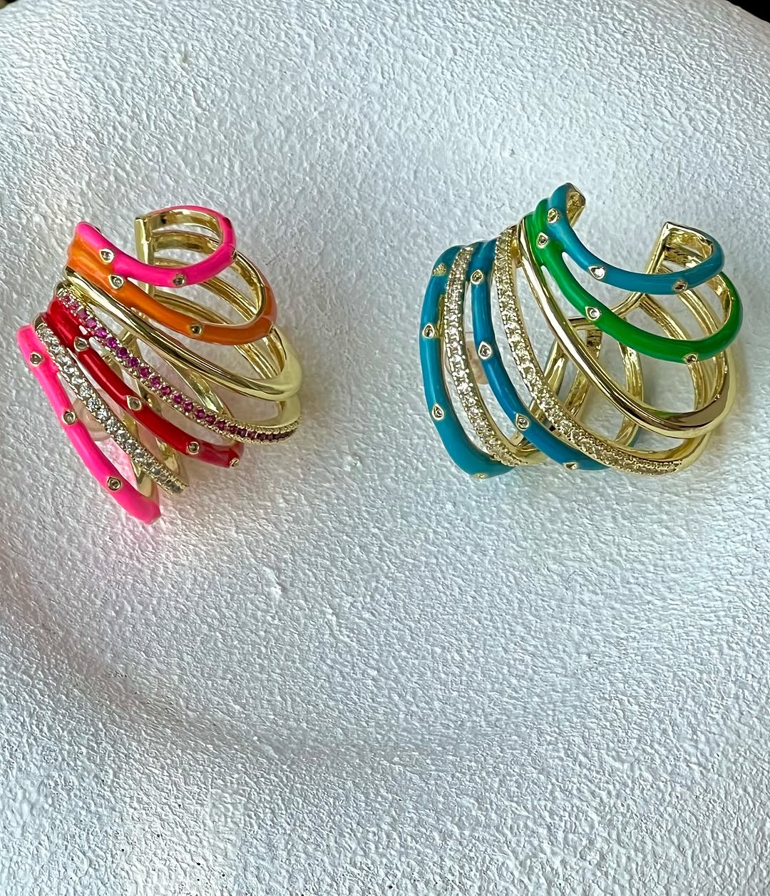 Dua ear cuff multirow enamel warna merah muda oranye dan biru hijau dengan bentuk jepitan terbuka di atas latar putih bertekstur