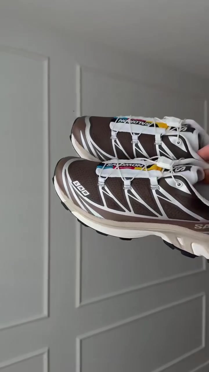 Sepasang Salomon XT-6 cokelat putih dipegang menghadap kamera, tampak sistem quicklace dan chassis samping