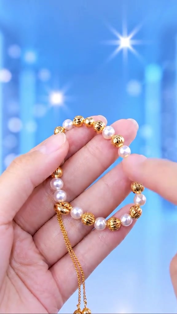 Tangan memegang gelang butiran mutiara putih berselang manik emas dengan rantai serut