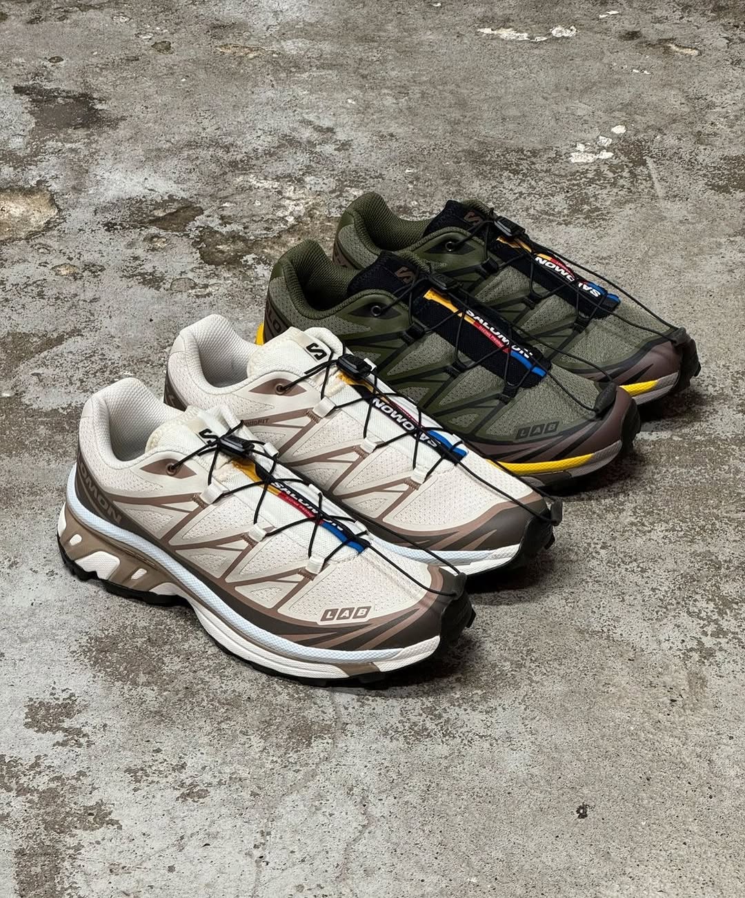 Dua pasang Salomon XT-6 warna krem dan hijau zaitun berjajar di lantai beton