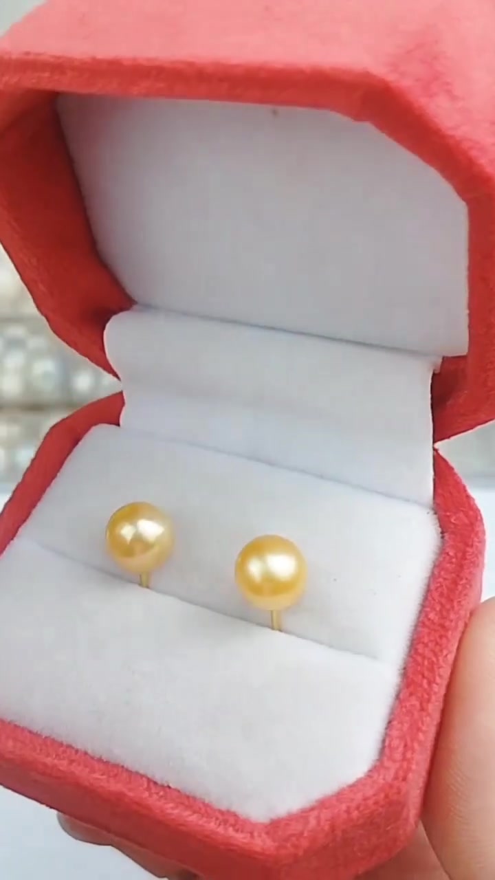Sepasang anting pentol mutiara keemasan di dalam kotak perhiasan merah muda yang dipegang tangan