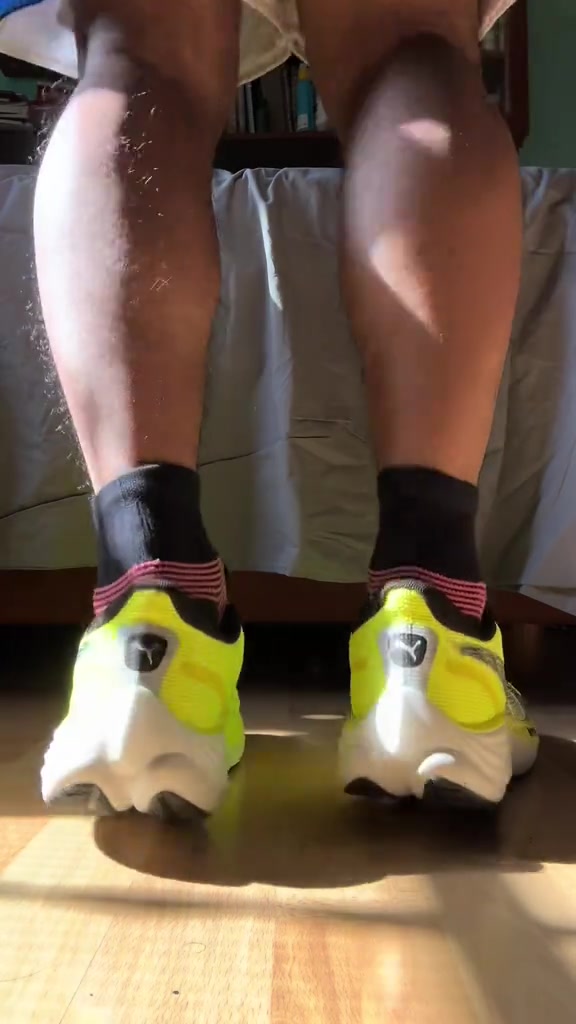 Tampak belakang sepasang sepatu lari Puma Velocity Nitro kuning dikenakan dengan kaus kaki hitam