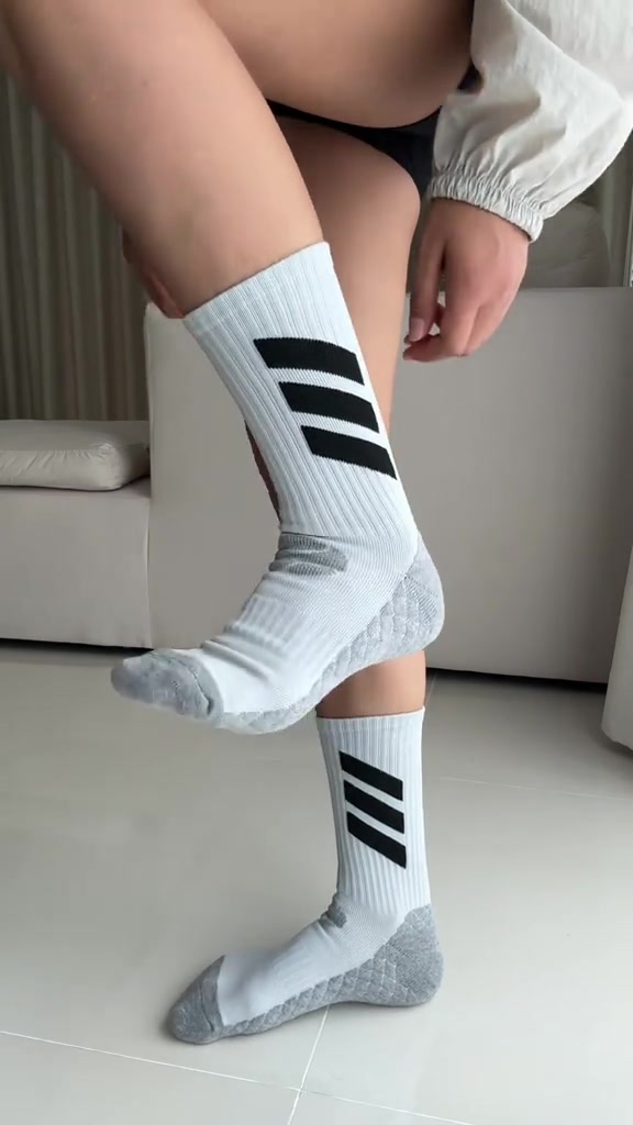 Try-on kaos kaki lari crew putih berajut tebal dengan aksen garis hitam di kaki, difoto di dalam ruangan tanpa sepatu