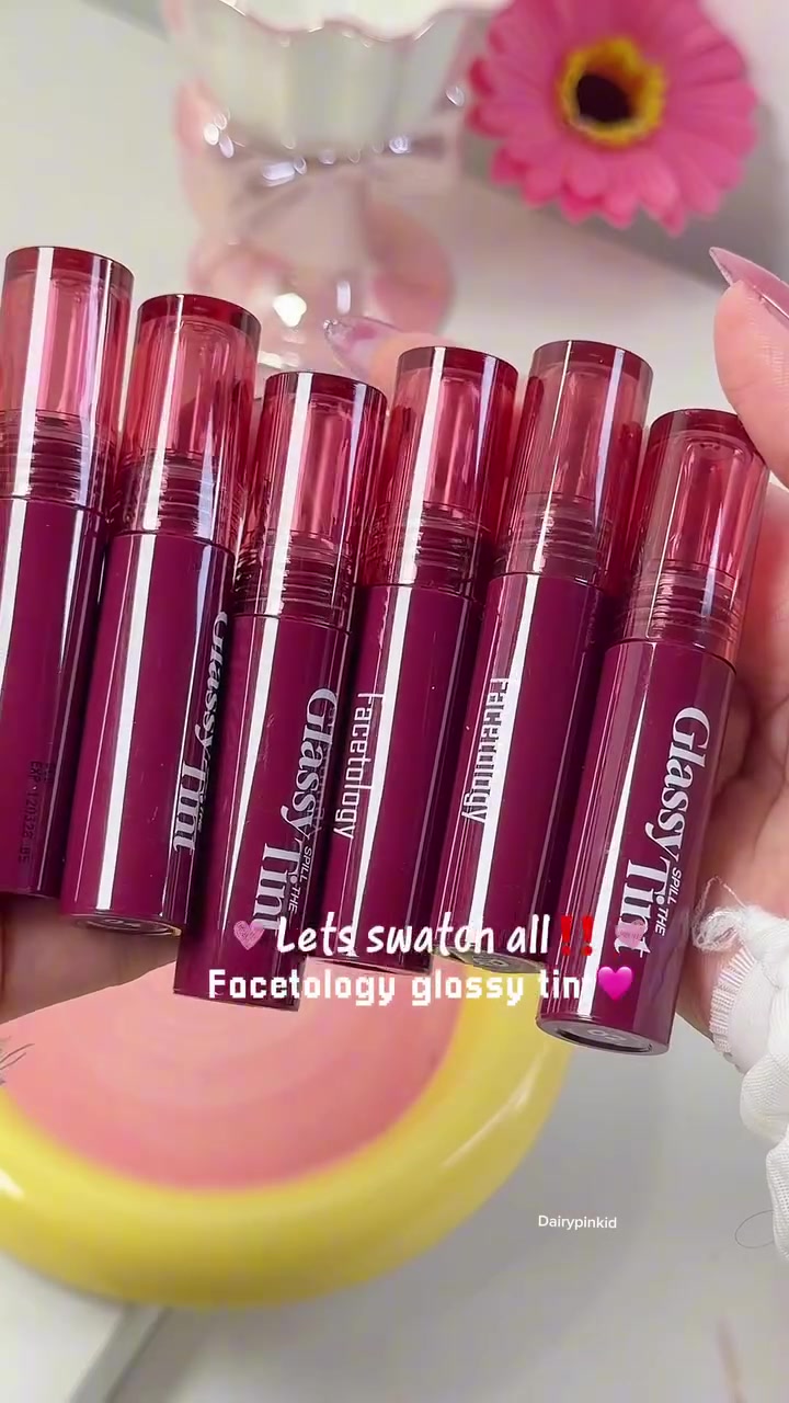 Enam tube Facetology Glassy Spill The Tint warna marun dipegang di atas piring kuning dan pink
