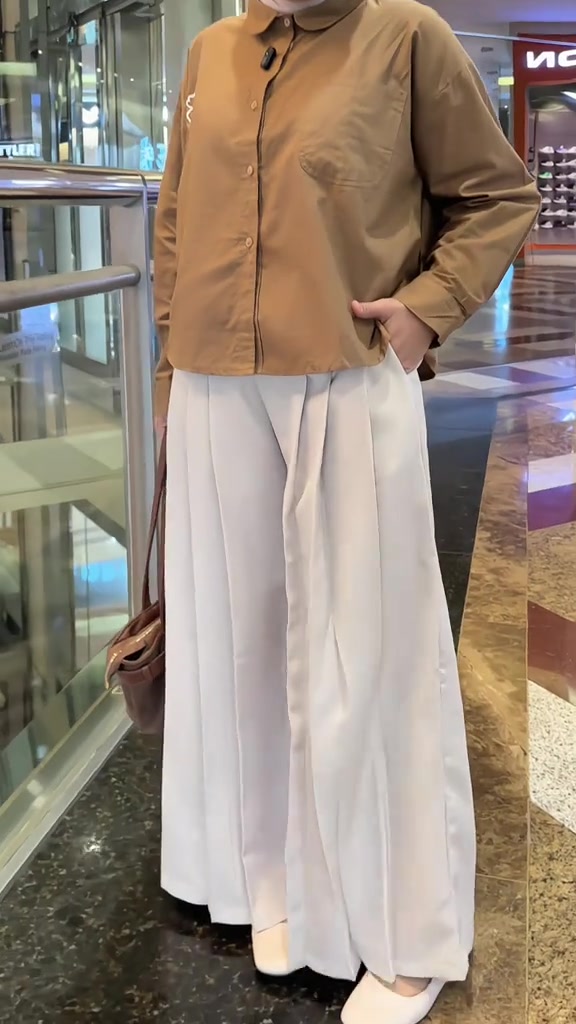 Kulot palazzo ivory dengan lipitan depan dipadukan kemeja coklat camel dan tas jinjing, tangan masuk saku, di koridor mal