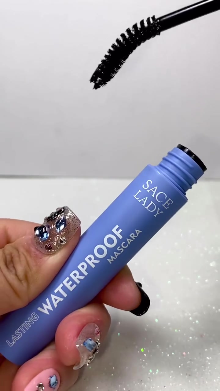 Tube maskara biru SACE LADY bertuliskan Lasting Waterproof Mascara dipegang tangan, dengan brush hitam melengkung di atasnya
