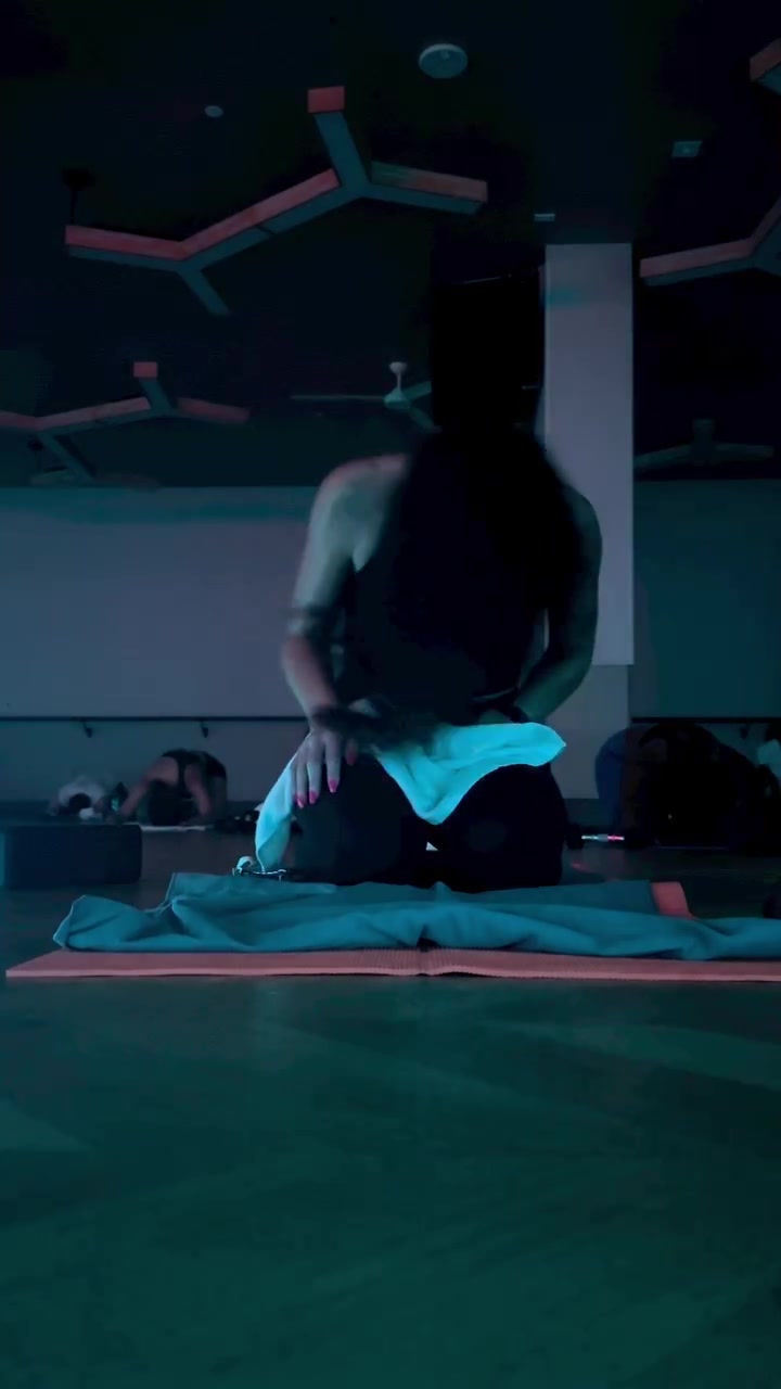 Peserta kelas hot mat tampak dari belakang berlutut di atas matras sambil mengikatkan handuk di pinggang di studio bercahaya redup