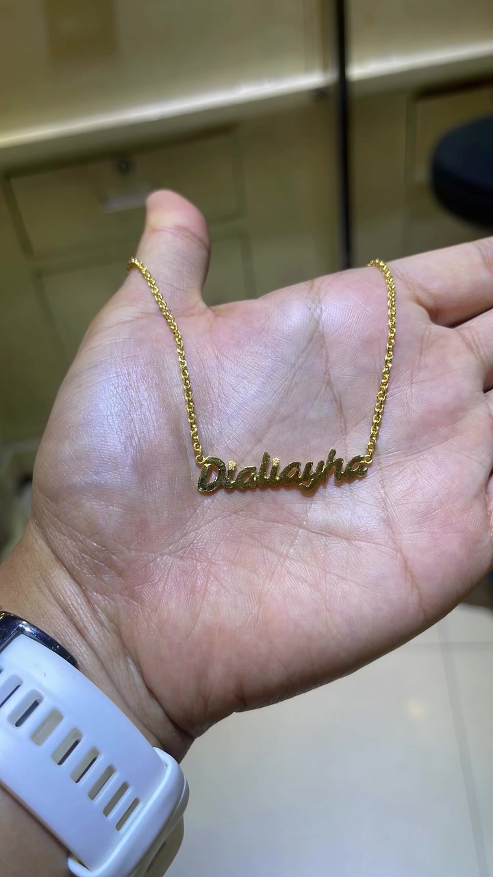 Kalung nama custom huruf script warna gold terbentang di telapak tangan