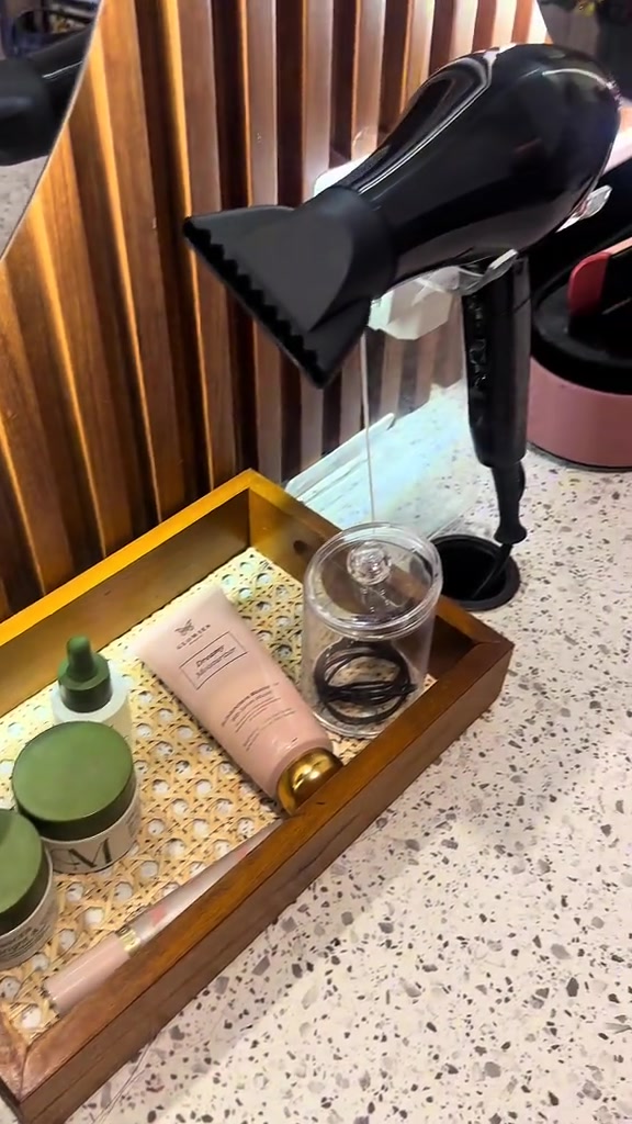 Meja rias studio dengan hair dryer, ikat rambut, dan toiletries tersusun di nampan kayu
