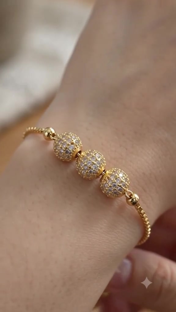 Close-up gelang serut emas dengan tiga bola pavé di pergelangan tangan