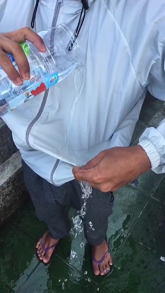 Tangan menuang air dari botol ke permukaan jaket putih tipis, air mengalir jatuh tanpa meresap ke kain