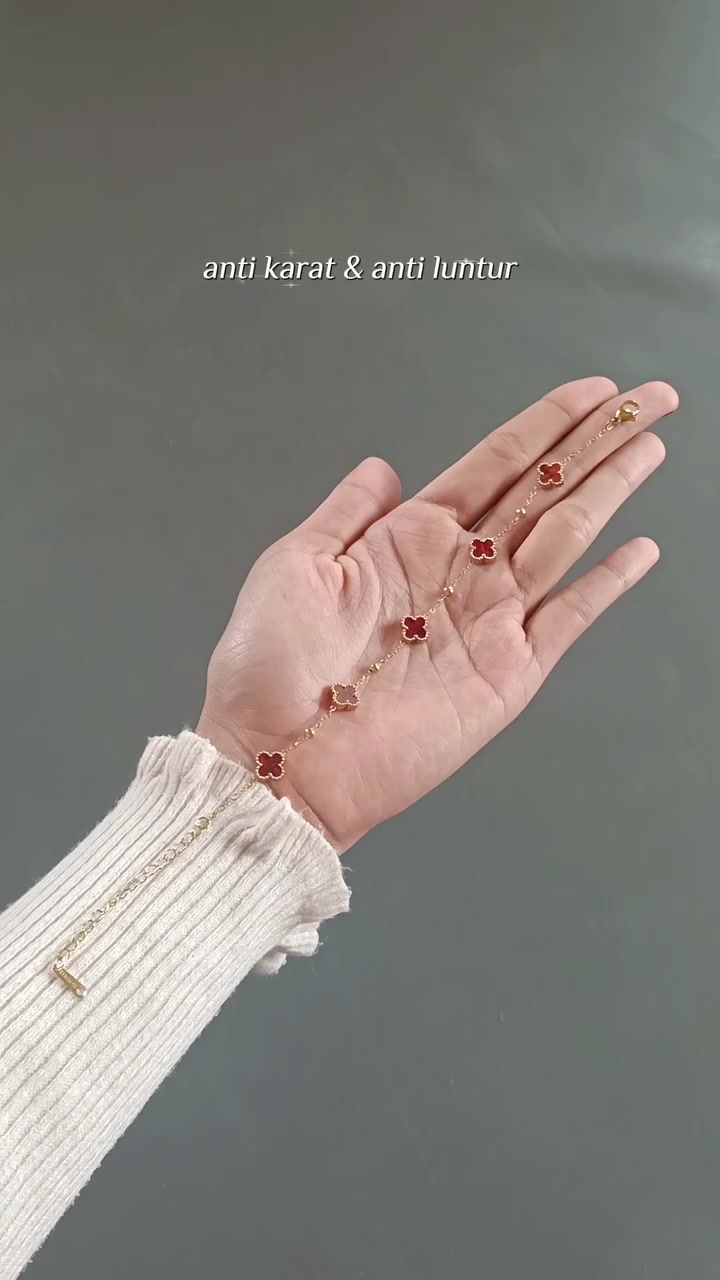 Gelang rantai clover merah melintang di telapak tangan dengan latar abu-abu