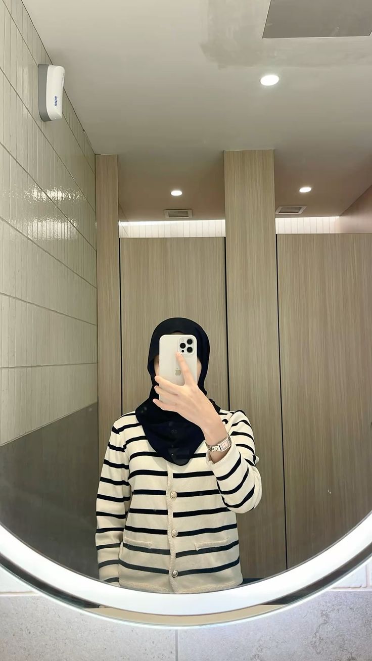 Swafoto cermin tanpa wajah: hijab hitam dengan cardigan krem garis-garis hitam berkancing di depan cermin bulat