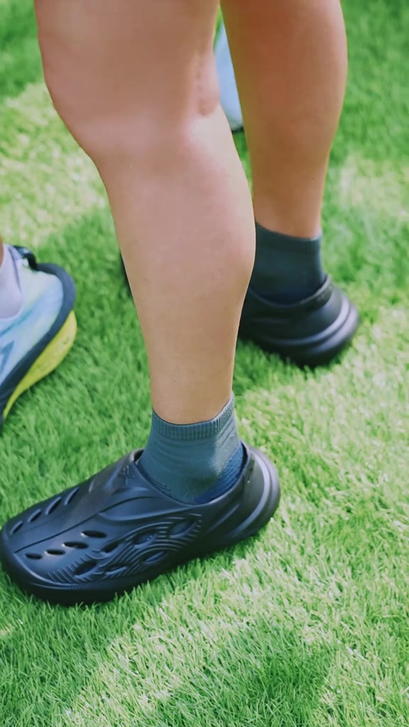 Sandal recovery model tertutup warna hitam dipakai berdiri di atas rumput sesudah lari