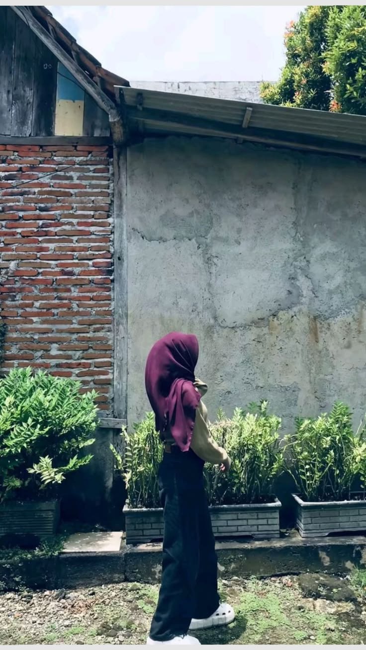 Tampak belakang perempuan berhijab maroon dengan atasan olive dan celana hitam potongan lebar yang jatuh menutup sepatu putih