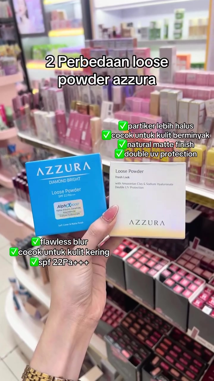 Tangan memegang dua box Azzura Loose Powder, varian biru Diamond Bright dan putih Fresh Look, di depan rak toko kosmetik