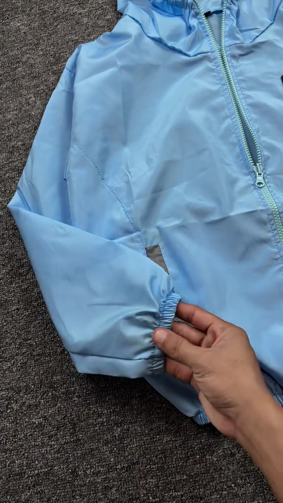 Detail manset elastis dan strip reflektif pada lengan jaket parasut biru muda yang dipegang satu tangan