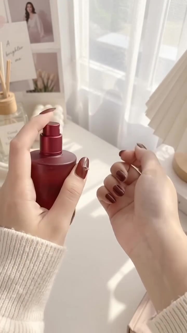 Dua tangan menyemprotkan botol parfum Scarlett X Soul berwarna merah di meja putih dekat jendela