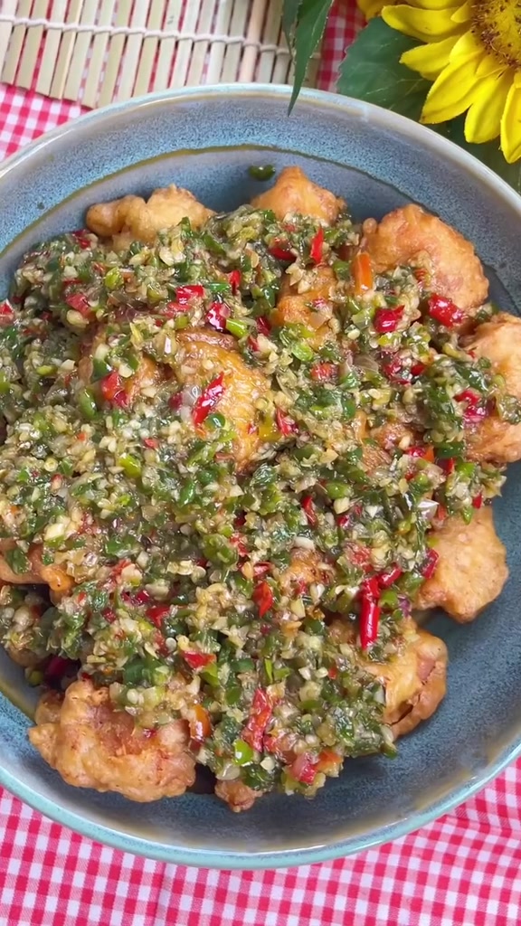 Mangkuk ayam goreng krispi berselimut sambal cabai hijau dan merah cincang kasar di atas kain kotak kotak merah