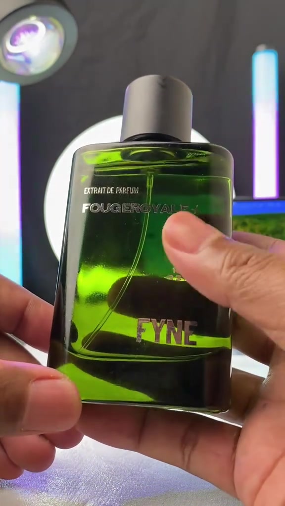 Dua tangan memegang botol kaca hijau Fyne Fougeroyale+ dengan latar lampu studio yang blur