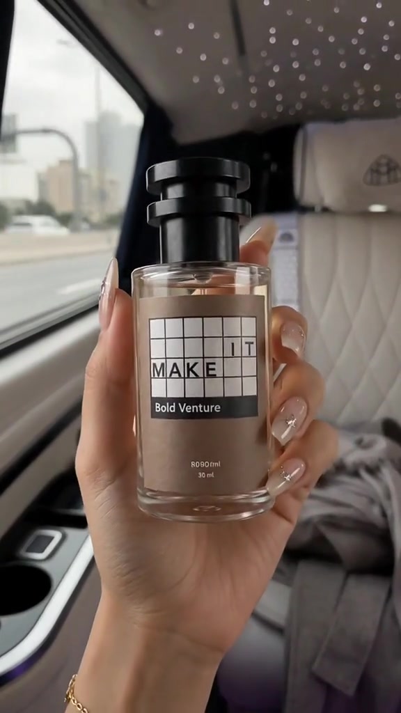 Tangan memegang botol Make It Bold Venture berlabel cokelat di dalam mobil berinterior terang