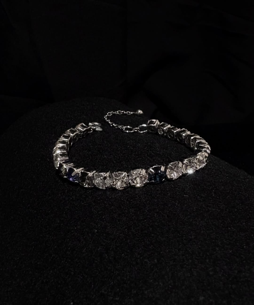 Tennis bracelet kristal disusun melingkar di kain hitam dengan rantai pemanjang di ujungnya
