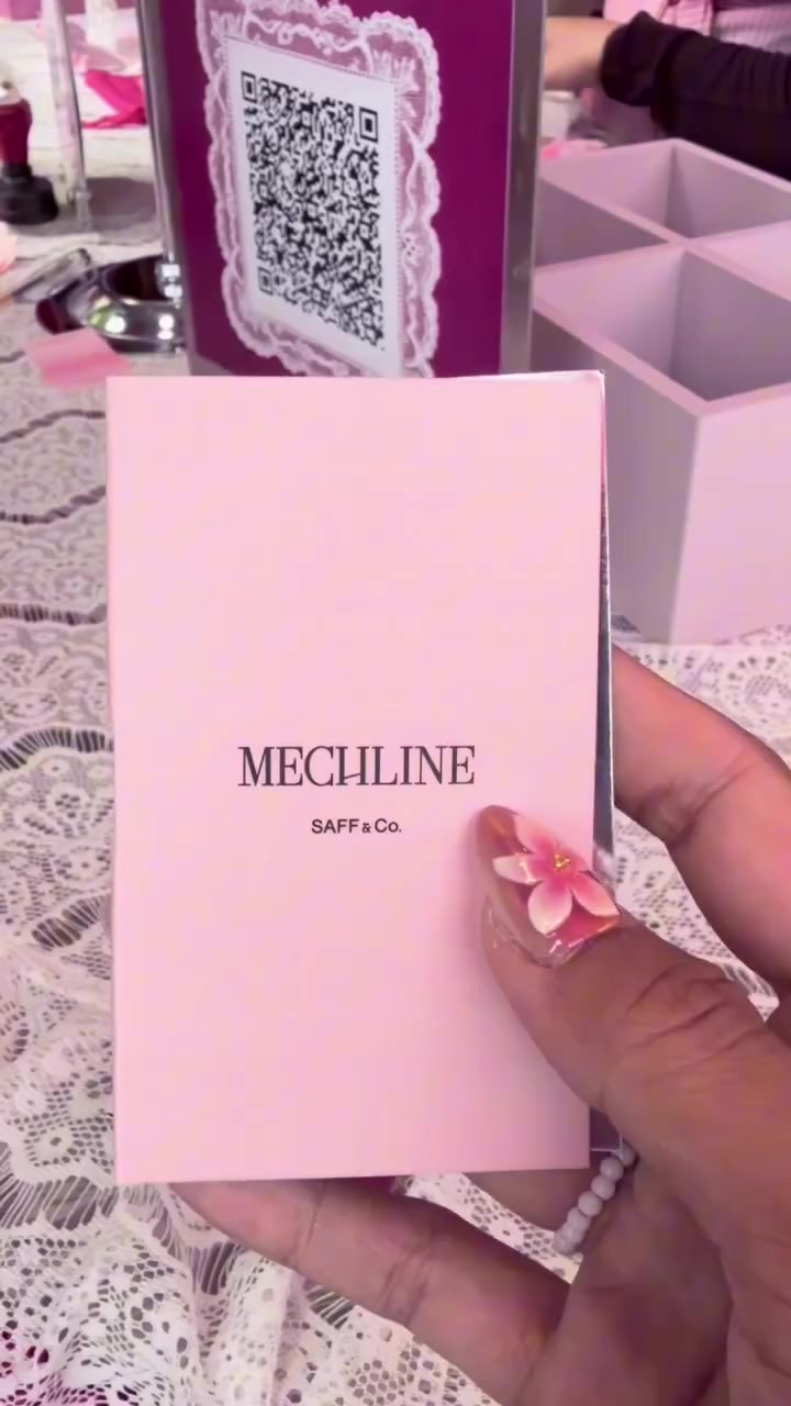 Tangan memegang kartu aroma Mechline dari SAFF & Co di atas meja renda pada pop-up The Pink Society
