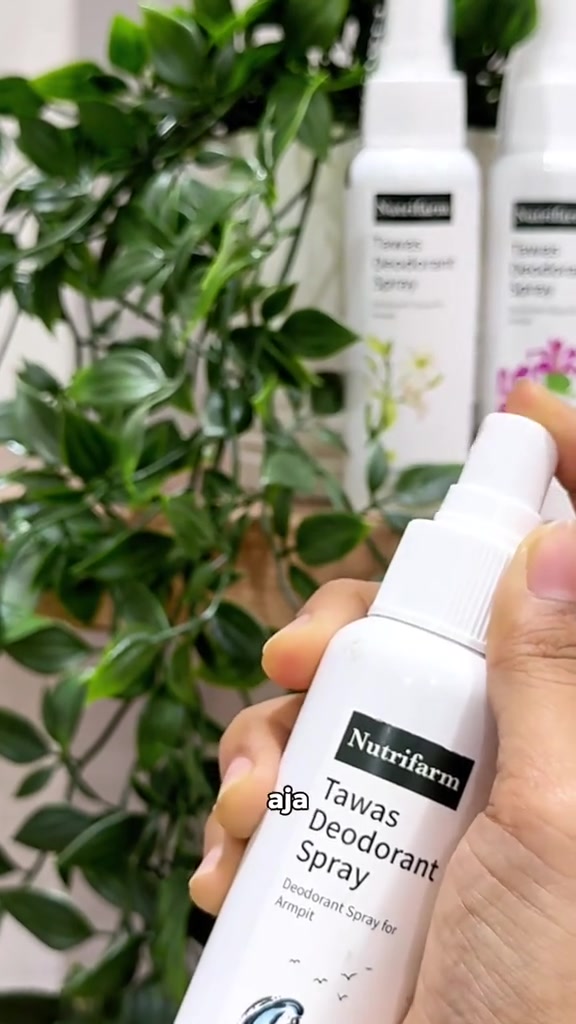 Tangan memegang botol Nutrifarm Tawas Deodorant Spray di depan tanaman hijau