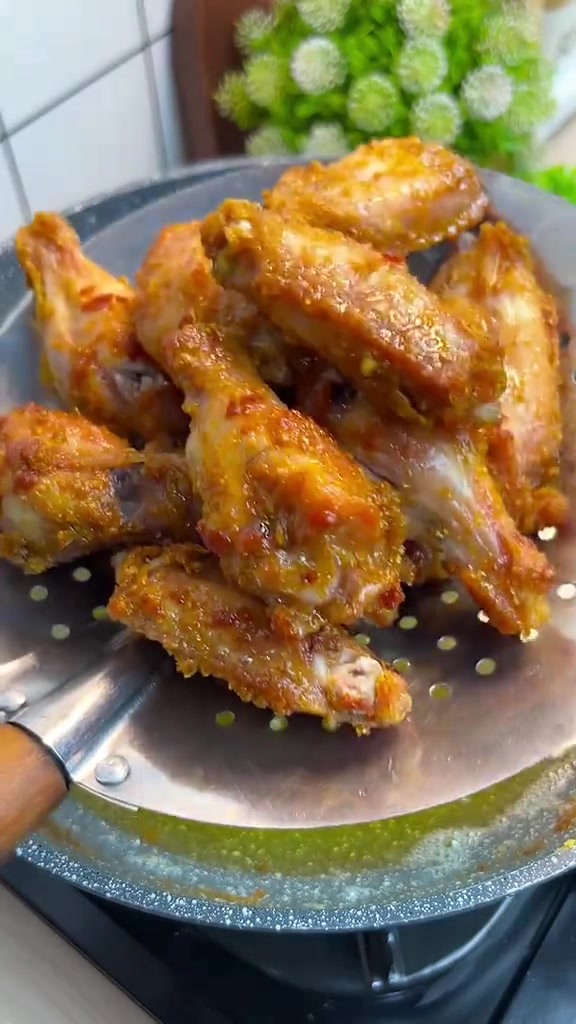 Sayap ayam goreng keemasan yang baru diangkat dan ditiriskan di saringan besi di atas wajan
